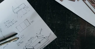 Mains anonymes esquissant des plans de rénovation avec règle et échantillons de matériaux