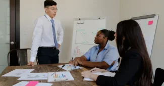 Personne présentant un projet structuré à des collègues autour d'une table avec schémas et notes