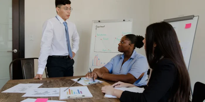 Personne présentant un projet structuré à des collègues autour d'une table avec schémas et notes