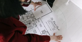 Mains anonymes examinant des plans et documents immobiliers sur un bureau ensoleillé