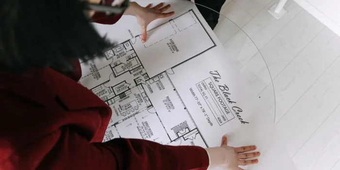 Mains anonymes examinant des plans et documents immobiliers sur un bureau ensoleillé