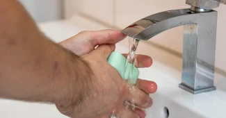 Mains gantées nettoyant un siphon d'évier avec outils posés à côté