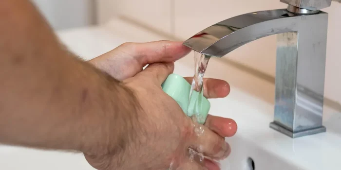 Mains gantées nettoyant un siphon d'évier avec outils posés à côté