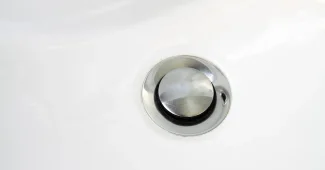 Main gantée retirant la grille d’un évier pour inspecter un siphon bouché