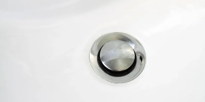 Main gantée retirant la grille d’un évier pour inspecter un siphon bouché