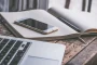 Personne utilisant un smartphone pour consulter les réseaux sociaux, avec un ordinateur portable et un carnet de notes s