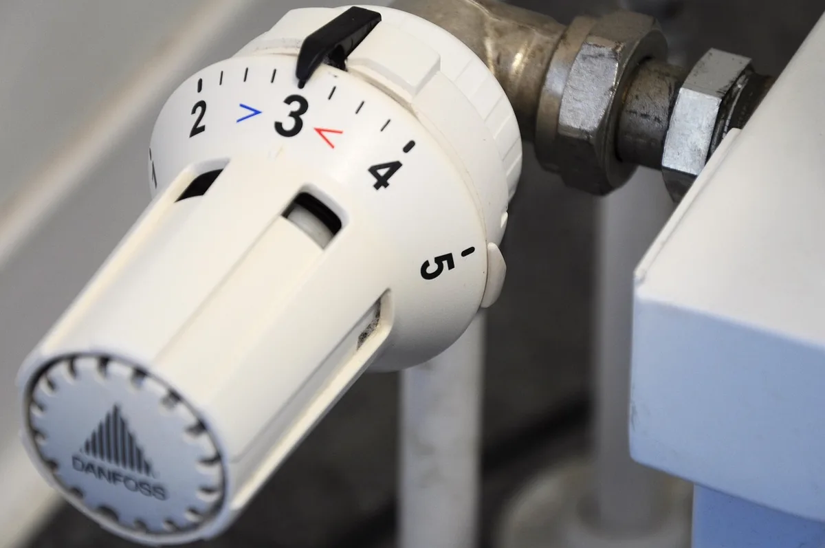 Personne ajustant un thermostat près d'une fenêtre, documents de consommation sur la table